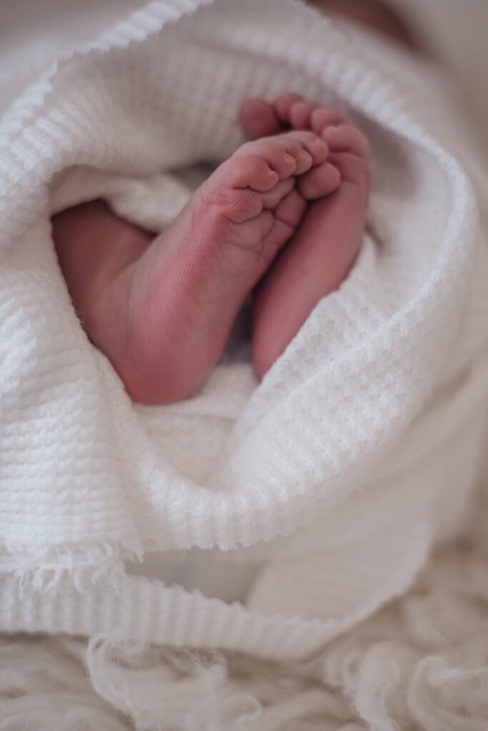 Pieds de nouveau‑né enveloppés dans une couverture blanche, photographie lifestyle en lumière douce.