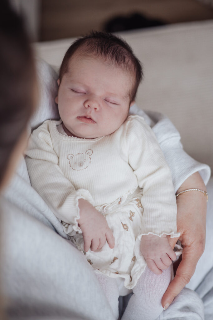 Nouveau‑né endormi dans les bras de sa maman, photographie lifestyle en lumière douce a domicile aux Sables d'Olonnes
