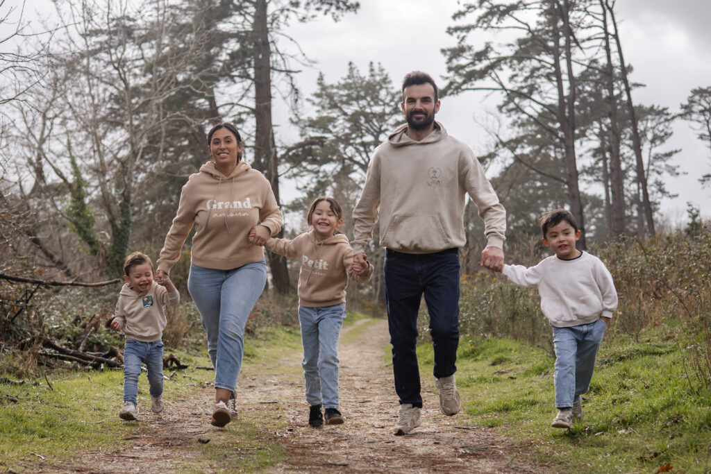 Séance photo avec une famille marchant main dans la main sur un chemin forestier, scène douce et naturelle.