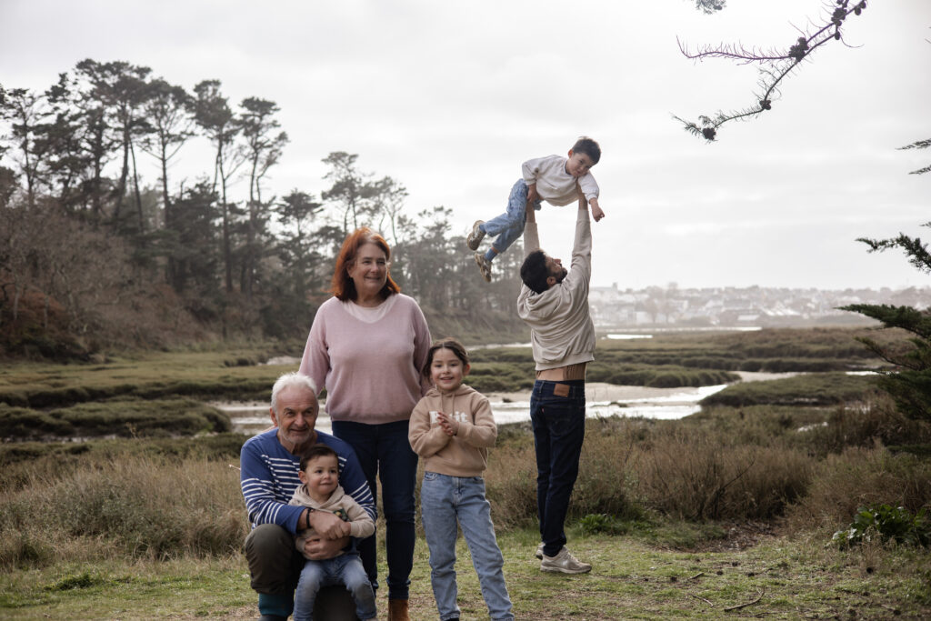 Famille réunie en extérieur près de l’eau pour un séance photo, moment joyeux capturé en lumière naturelle.