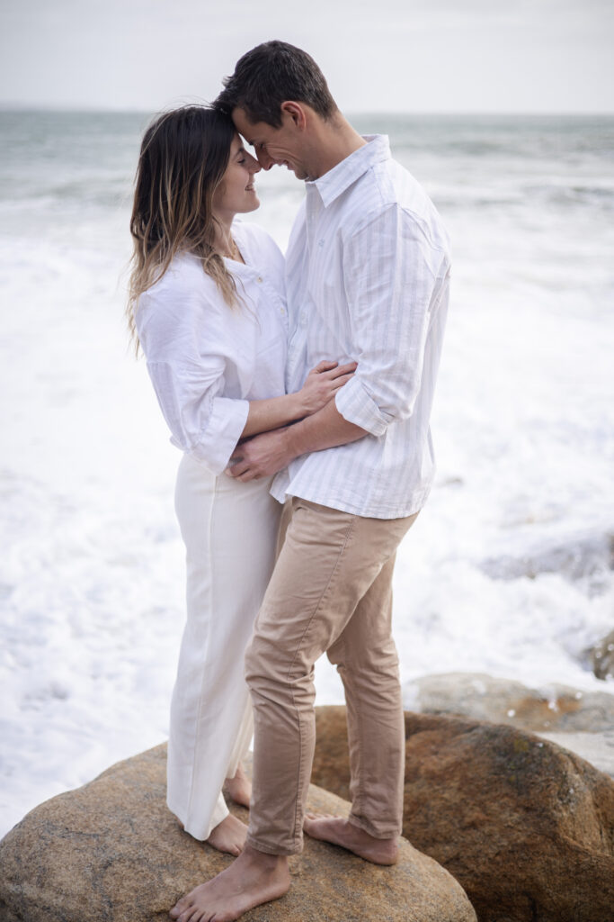 Couple enlacé sur un rocher au bord de l’océan, scène intime en lumière douce.