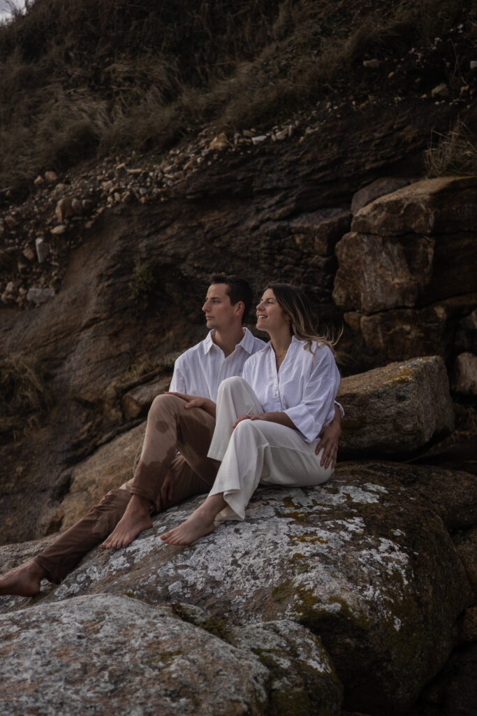 Couple assis sur les rochers près de la falaise, moment calme et contemplatif en bord de mer.