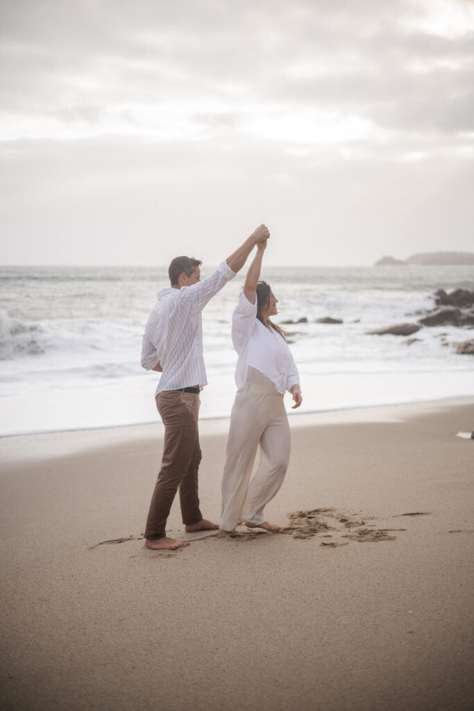 Séance photo d'un couple dansant pieds nus sur la plage, moment joyeux capturé en lumière naturelle.
