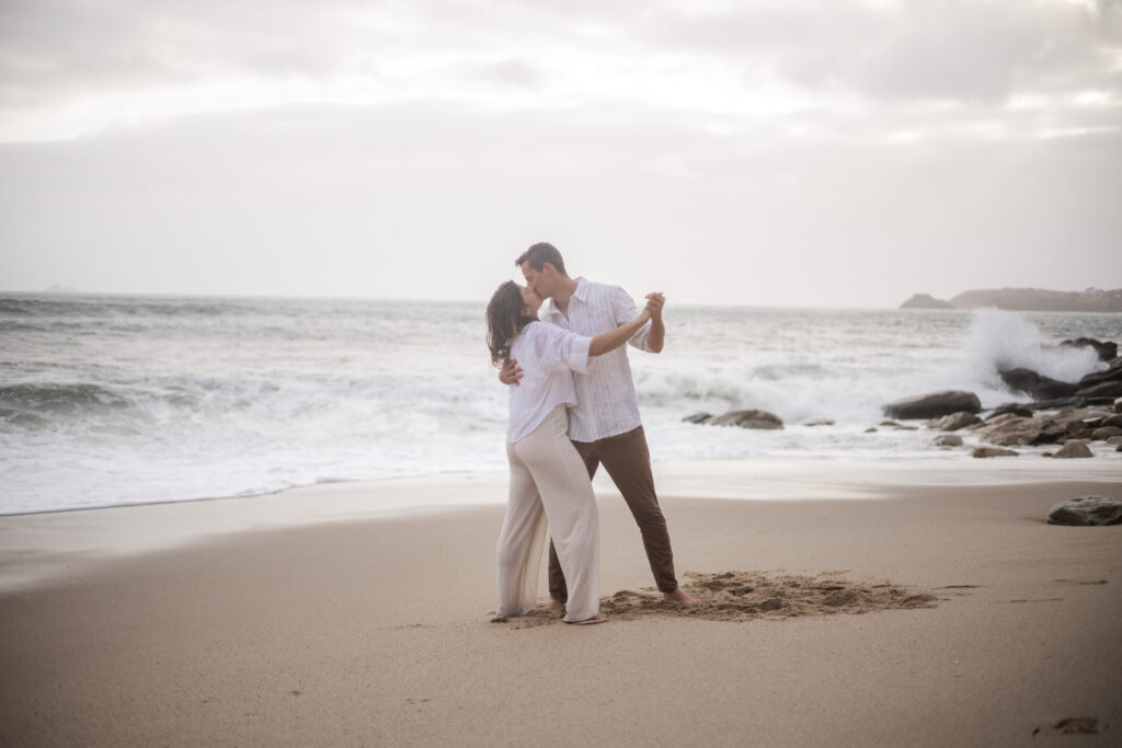 Couple s’embrassant sur la plage, scène romantique en bord de mer en lumière douce.