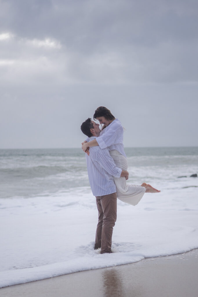 Couple souriant dans les vagues, l’homme portant sa partenaire, scène lumineuse en bord de mer.