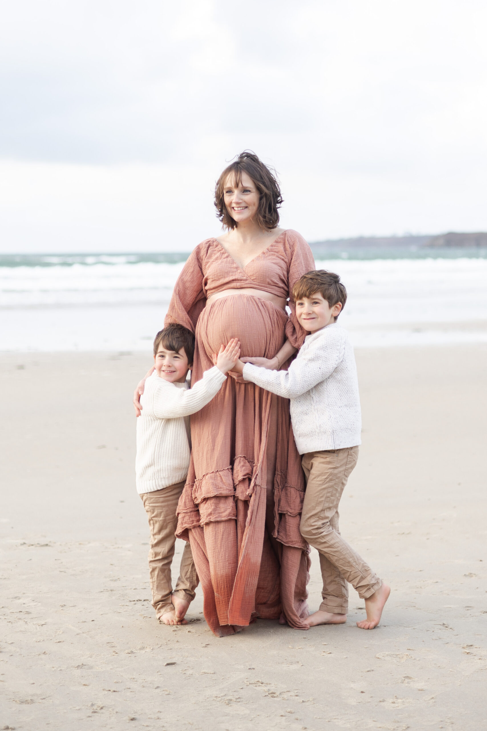 femme enceinte avec ses deux premiers enfants sur le sable, pendant une séance grossesse en exterieur
