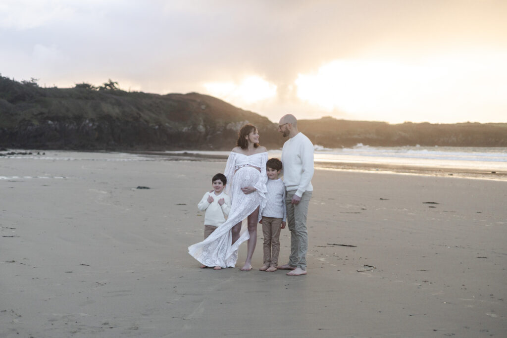 Famille photographiée sur la plage près des Sables‑d’Olonne, pendant une séance grossesse, moment tendre en lumière naturelle.